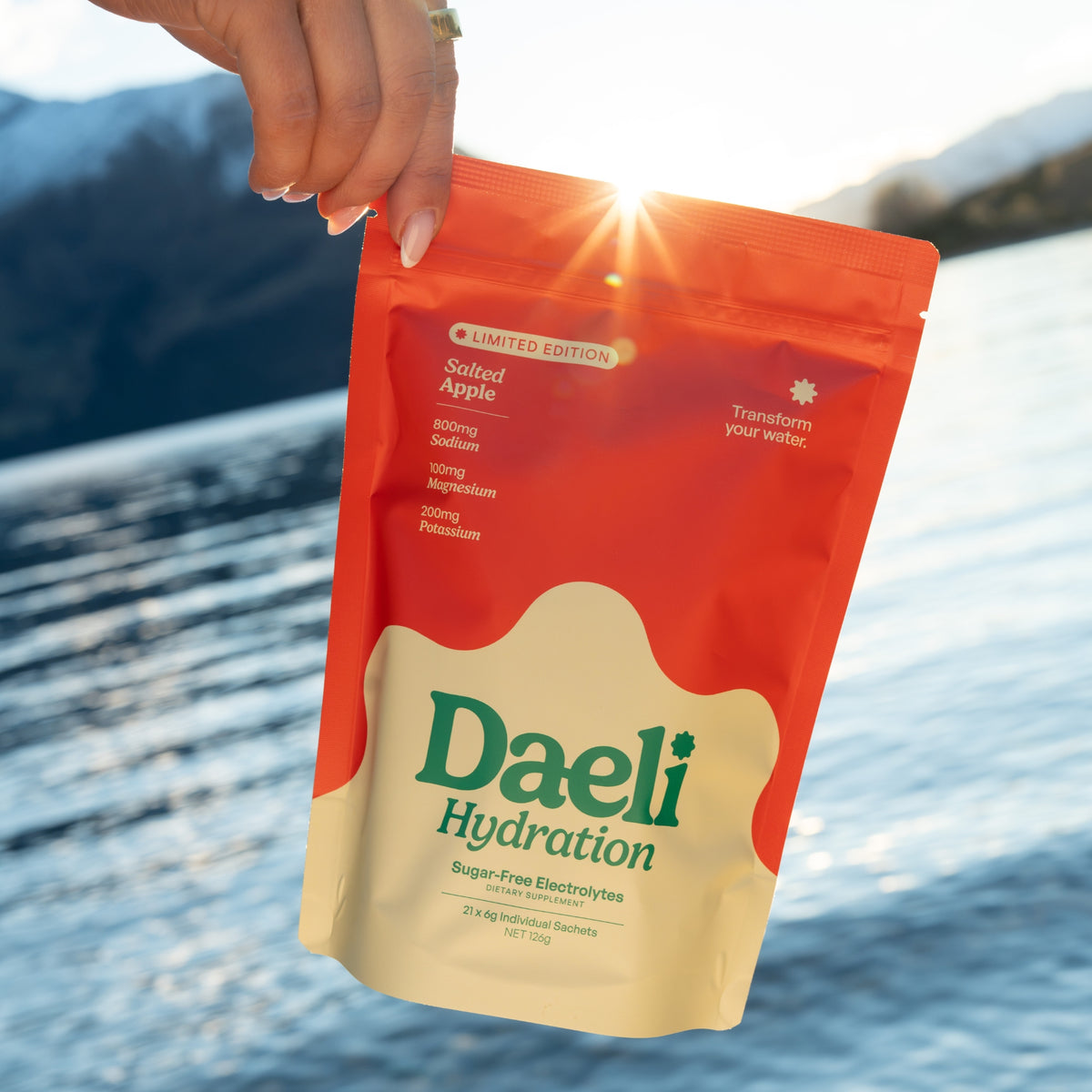 Daeli Hydration Salted Apple pouch being held by someone in front of a lake.