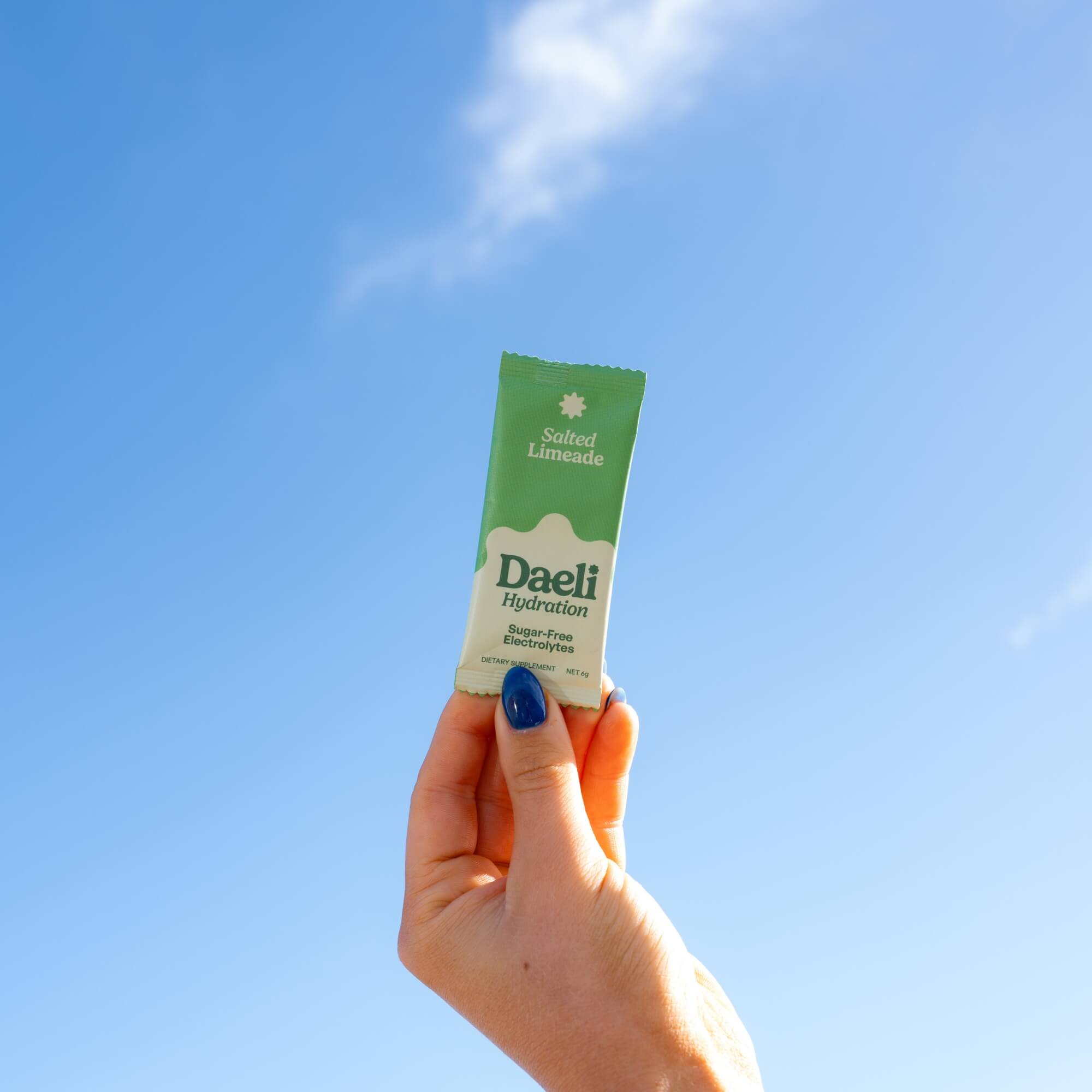 Hand holding Daeli Salted Limeade electrolyte sachet against a bright blue sky - refreshing hydration for everyday energy.