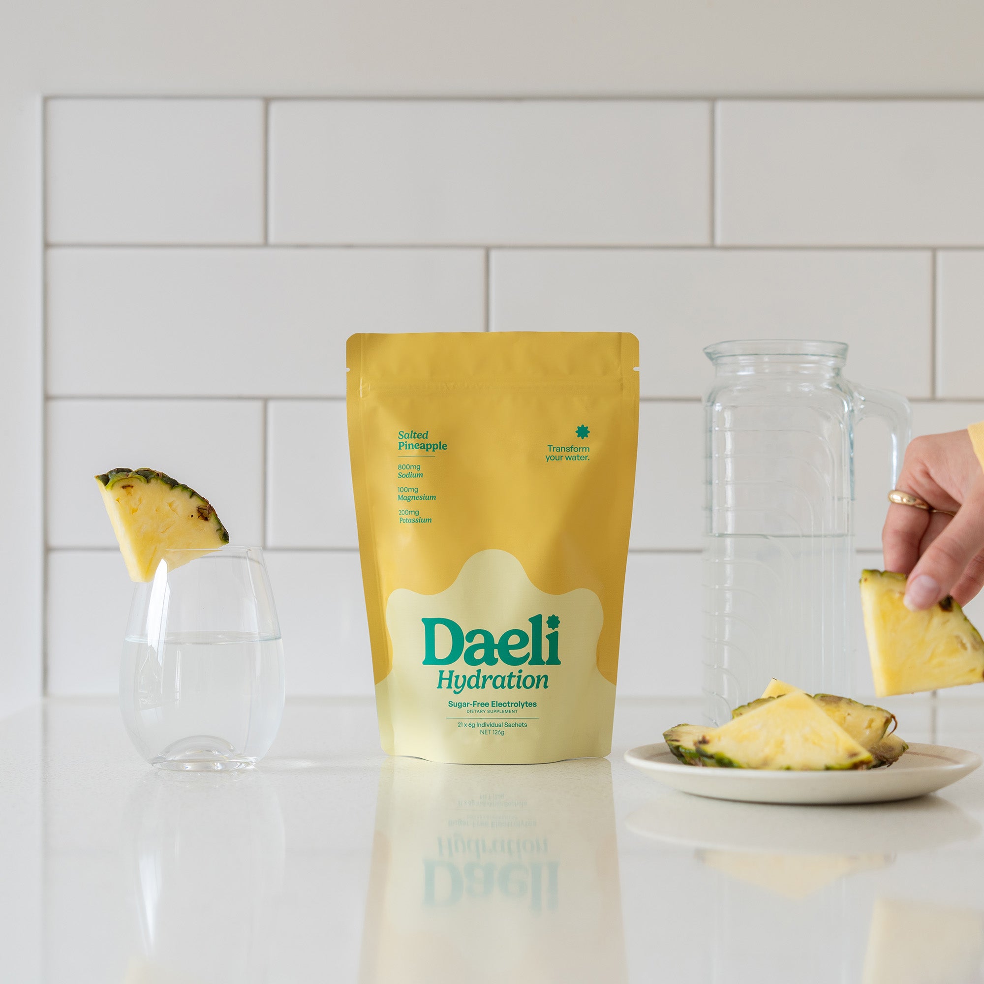Daeli Hydration Salted Pineapple electrolyte pouch on a kitchen counter with pineapple slices and a glass of water