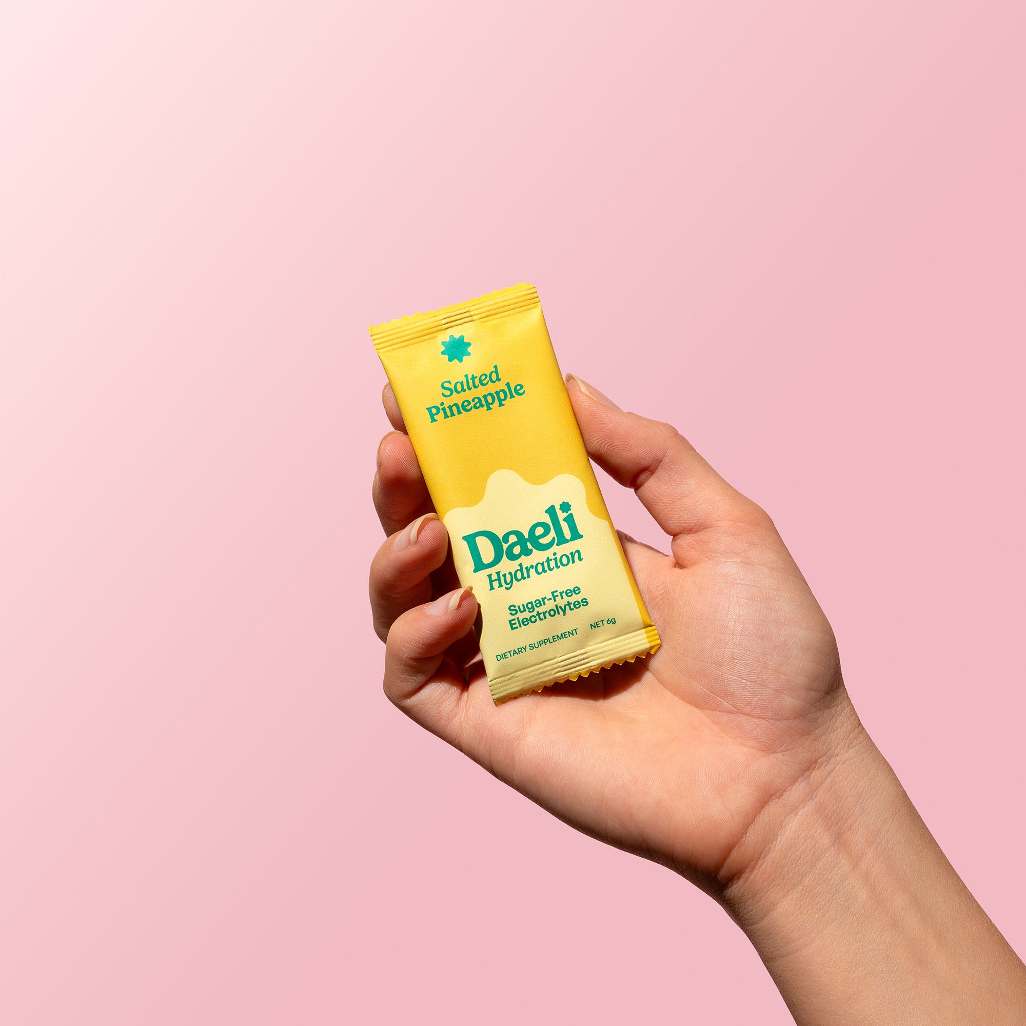 Hand holding Daeli Hydration Salted Pineapple electrolyte sachet against a soft pink background - on the go sugar-free hydration.