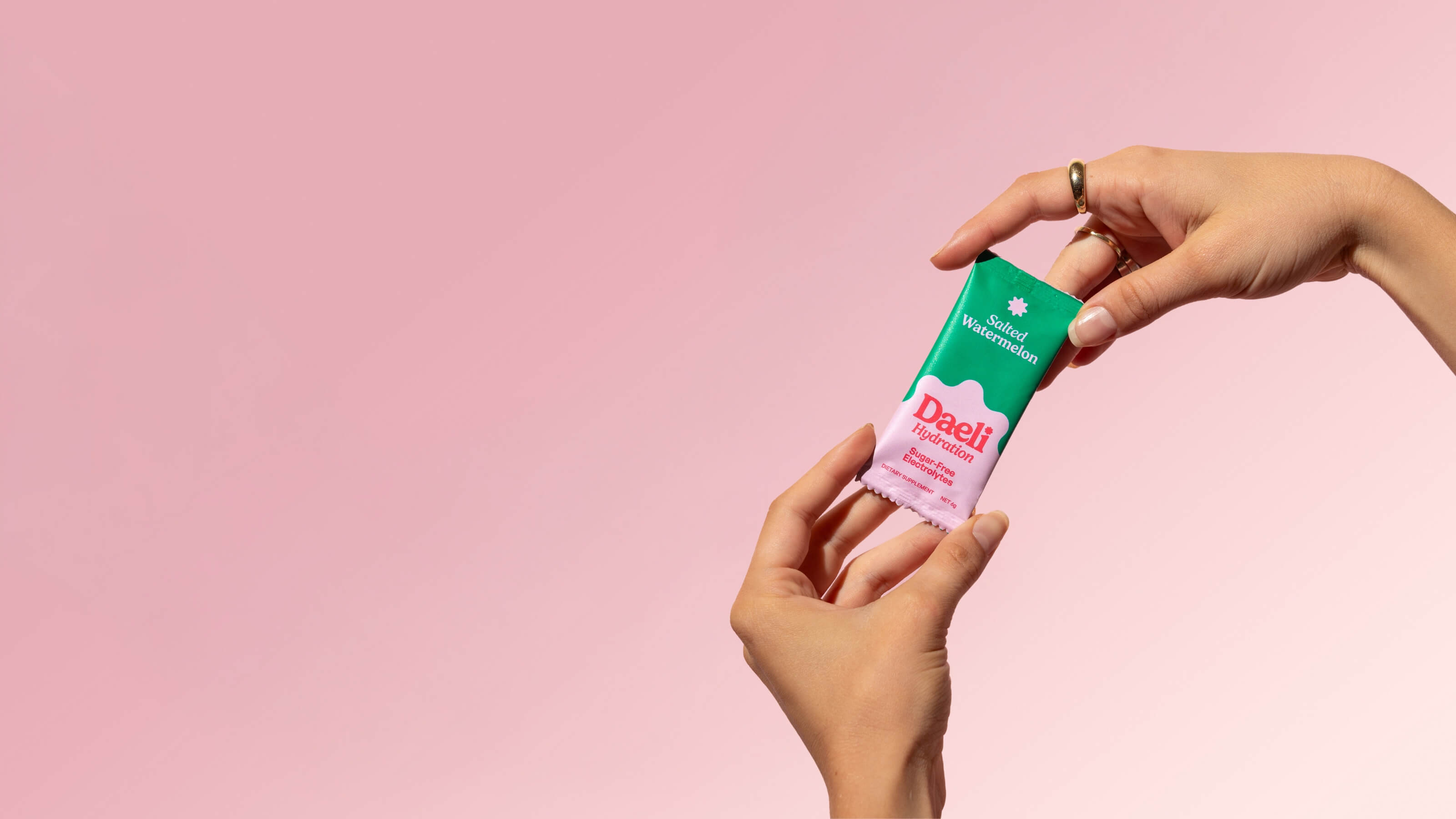 Daeli Journal - Hands holding Daeli Hydration Salted Watermelon electrolyte sachet against a soft pink background - glamorous hydration, styled for desktop.