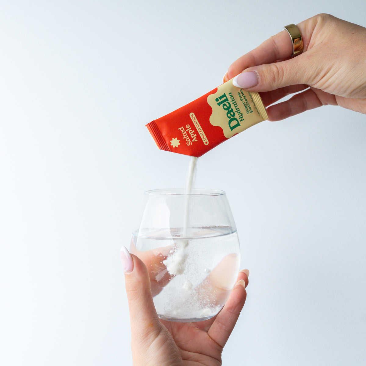 Hand pouring Daeli Hydration Salted Apple electrolyte powder into a glass of water.