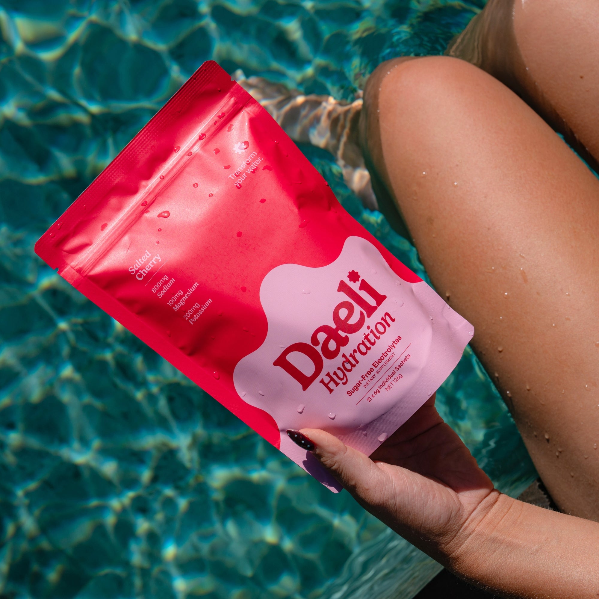 Daeli Hydration Salted Cherry pouch being held by someone with their legs in the pool.