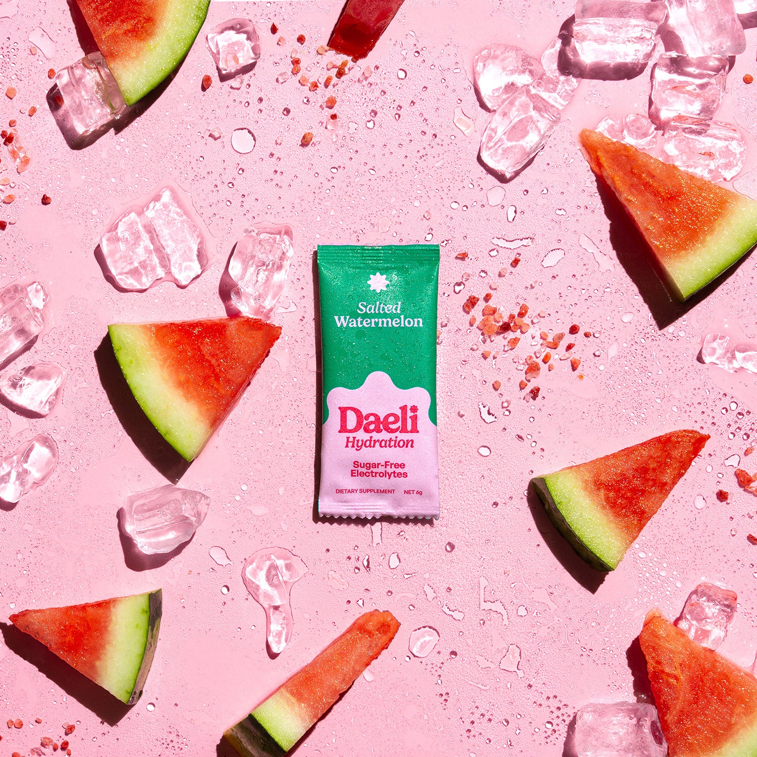 Daeli Hydration Salted Watermelon electrolyte sachet surrounded by watermelon slices, ice, and salt on a pink surface - vibrant and hydrating flavour burst.